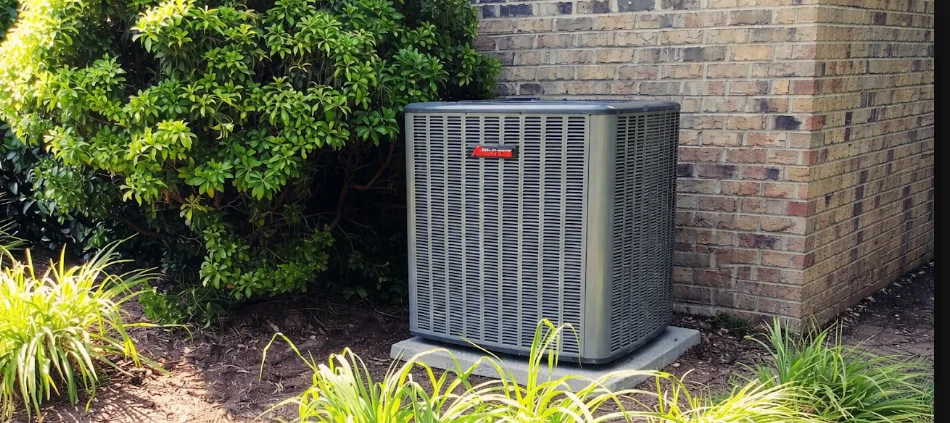 A newly installed HVAC outdoor condenser unit positioned on a concrete pad beside a single-family home in a Greenville, SC residential neighborhood. The unit is connected and ready for operation, with a clean line set running along the exterior wall.